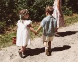 Zwei Kinder, ein Mädchen mit Blumenkranz und ein Junge, halten Händchen auf dem Weg zu einer Hochzeit mit Kindern.