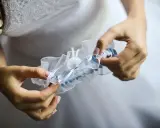 Braut hält ein weißes Strumpfband mit blauen Akzenten. Das Strumpfband ist ein traditionelles Symbol für Glück bei der Hochzeit.