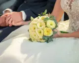 Brautpaar hält Händchen, Brautstrauß mit gelben Rosen. Eine Hochzeit Versicherung gibt Sicherheit für den großen Tag.