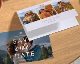 Hochzeitseinladungskarten mit Foto: Ein Paar küsst sich vor Bergkulisse, daneben eine Einladung zur Hochzeit mit drei Fotos des Paares.