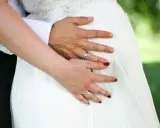 Hände auf dem Bauch einer schwangeren Braut im weißen Kleid. Ein Paar heiratet voller Vorfreude.