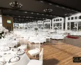 Elegante Glashaus Hochzeitslocation mit vielen weiß gedeckten Tischen, weißen Stühlen und üppigen Blumenarrangements.