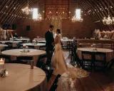 Ein Brautpaar steht sich in einem rustikalen Saal gegenüber, der für eine minimalistische Hochzeit mit Lichterketten und Kerzen dekoriert ist.