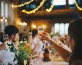 Gäste stoßen mit Sekt an, Lichterketten leuchten. Eine Einladung zur after wedding party.