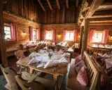 Gemütliche Holzhütte, festlich gedeckte Tische für eine Egerner Alm Hochzeit. Rote Karovorhänge und Blumen schmücken den rustikalen Raum.
