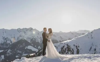 Ein Brautpaar steht sich in der verschneiten Berglandschaft gegenüber. Ihre **Hochzeit im Schnee** ist ein magischer Moment vor der Kulisse schneebedeckter Gipfel.