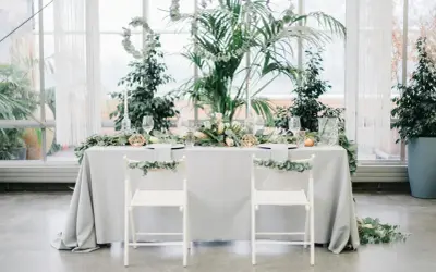 Ein festlich gedeckter Tisch für eine greenery hochzeit, umgeben von üppigem Grün. Zwei weiße Stühle mit Eukalyptus-Girlanden stehen bereit.