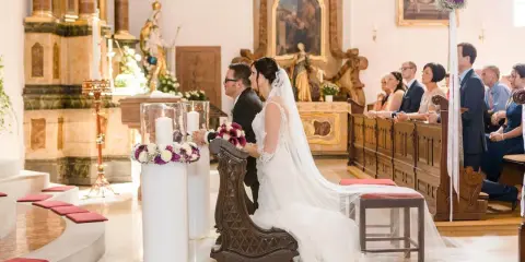 Brautpaar kniet vor dem Altar. Sie heiraten kirchlich, nur ein Partner in der Kirche. Gäste sitzen auf den Bänken.