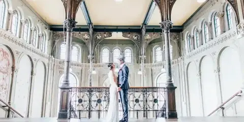 Ein Brautpaar im Stil der 20er Jahre steht sich in einem prachtvollen Gebäude mit Jugendstil-Architektur gegenüber.