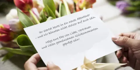 Hände halten eine Karte mit emotionalen Hochzeitswünschen vor einem Tulpenstrauß.