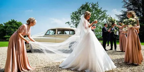 Brautjungfern helfen der Braut mit ihrem Schleier vor einer Hochzeitslimousine.
