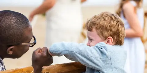 Ein Mann mit Brille hält die Hand eines Jungen. Im Hintergrund heiratet mein Sohn.