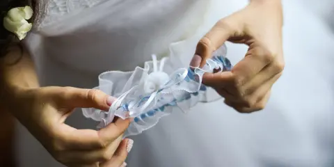 Braut hält ein weißes Strumpfband mit blauen Akzenten. Das Strumpfband ist ein traditionelles Symbol für Glück bei der Hochzeit.