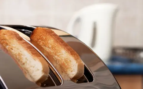 Zwei goldbraune Scheiben Toastbrot ragen aus einem glänzenden Toaster. Ein perfekter Moment, um einen Toast auszusprechen.