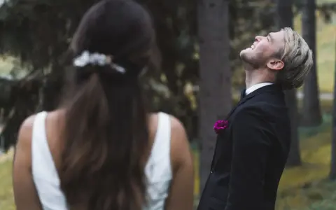 Ein Bräutigam lacht mit geschlossenen Augen in den Himmel, während die Braut ihm den Rücken zukehrt. Vielleicht ist es die Angst vor der Hochzeit, die ihn so überwältigt.