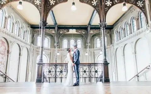 Ein Brautpaar im Stil der 20er Jahre steht sich in einem prachtvollen Gebäude mit Jugendstil-Architektur gegenüber.