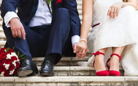 Brautpaar hält Händchen, rote Rosen und rote Schuhe. Die Frage "wie kurzfristig kann man heiraten" beschäftigt viele Paare.