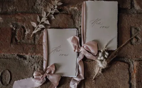 Zwei Büchlein mit zarten Bändern, auf denen "His vows" und "Her vows" steht, bereit, um Eheversprechen zu schreiben.