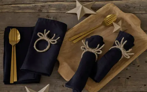 Serviettenringe selber machen: Dunkle Stoffservietten mit rustikalen Geweih-Motiven aus Jute, dazu goldene Besteckteile und Papiersterne.