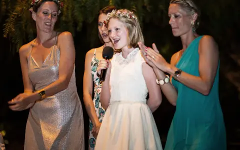 Mädchen hält Mikrofon, während ihre Schwester und andere Frauen bei einer Hochzeitsrede applaudieren.