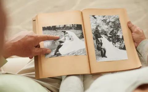 Ein älteres Paar blättert in einem Fotoalbum. Ein Finger zeigt auf ein Hochzeitsfoto. Wie viele Jahre ist die Gnadenhochzeit her?