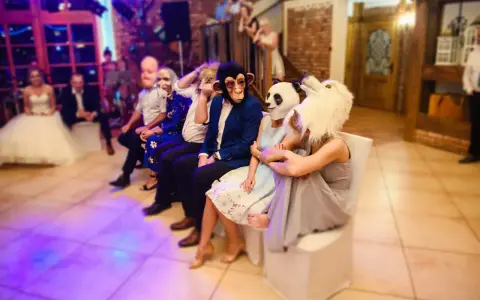 Gäste in Tiermasken warten auf kurzweilige Hochzeitsspiele. Ein Affe, ein Panda und ein weißes Tier sind zu sehen.