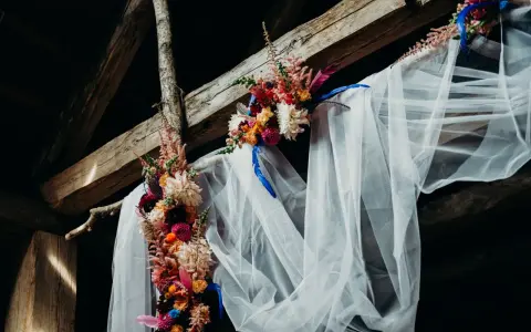 Blumenbogen mit Schleier unter Holzbalken, ein romantischer Ort für eine Feier, vielleicht zum 5 Jahre verheiratet Jubiläum.