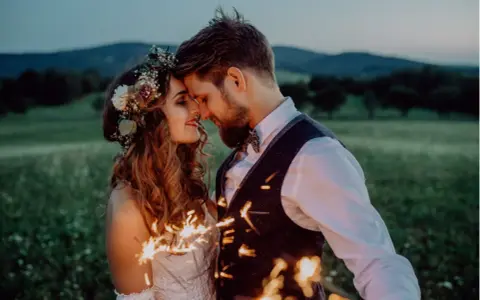 Ein Brautpaar feiert seine elopement hochzeit im Freien bei Einbruch der Dunkelheit mit Wunderkerzen.
