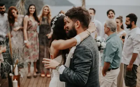 Glückliches Brautpaar umarmt sich, Gäste im Hintergrund. Perfekt für zitate hochzeitskarte.