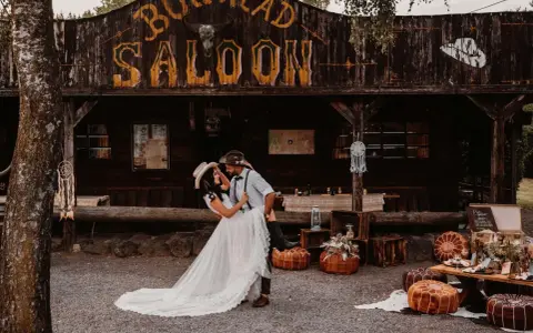 Ein Brautpaar feiert seine western hochzeit vor einem Saloon. Sie tanzen ausgelassen, umgeben von rustikaler Deko.