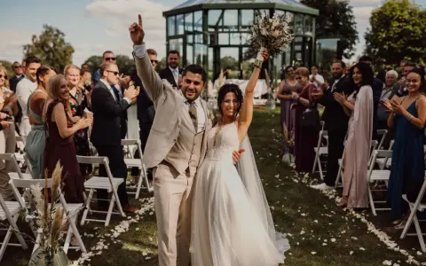 Glückliches Brautpaar feiert den Beginn des Hochzeitsablaufplans. Gäste applaudieren bei der Zeremonie im Freien.