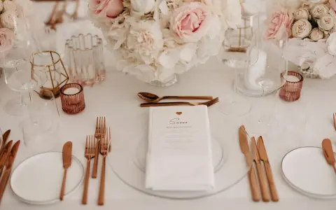 Ein festlich gedeckter Tisch mit Blumen, Gläsern und roségoldenem Besteck. Ein Hochzeitsmenü für Susan, perfekt arrangiert vom wedding planer.