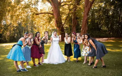 Brautjungfern in Polka-Dot-Kleidern und die Braut in Weiß posieren für eine fröhliche Rockabilly-Hochzeit im Freien.