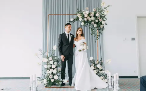 Ein Brautpaar steht vor einem floralen Bogen, bereit, wie heiratet man. Sie strahlen Glück aus.