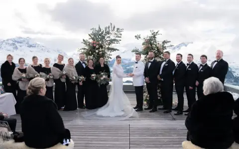 Brautpaar und Hochzeitsgesellschaft vor schneebedeckten Bergen. Eine wunderschöne Hochzeit in den Bergen mit Brautjungfern in schwarzen Kleidern und Männern in Anzügen.