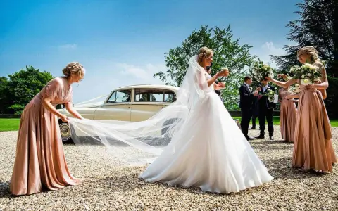 Brautjungfern helfen der Braut mit ihrem Schleier vor einer Hochzeitslimousine.