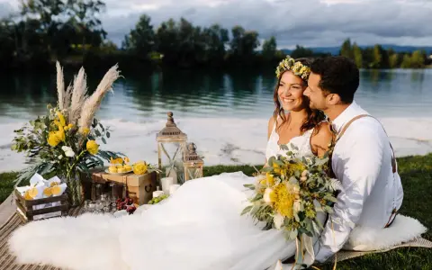 Glückliches Brautpaar genießt seine Hochzeit am See. Blumen, Laternen und ein Picknickkorb schaffen romantische Atmosphäre.