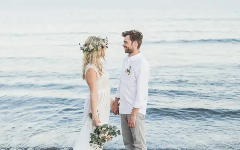 Ein glückliches Paar feiert seine Hochzeit am Strand zu zweit. Die Braut trägt einen Blumenkranz, der Bräutigam ein weißes Hemd.