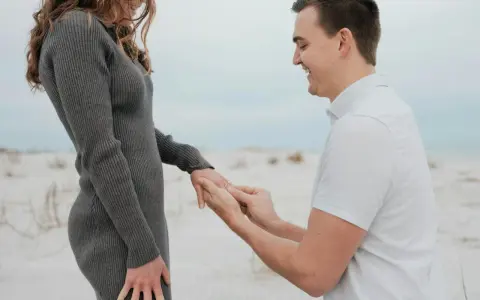 Ein Mann kniet am Strand und steckt seiner lachenden Partnerin einen Ring an den Finger. Ein Moment, der die tiefe **Verlobung Bedeutung** symbolisiert.
