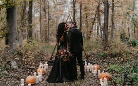 Ein Brautpaar küsst sich im Wald bei Kerzenlicht und Kürbissen. Eine romantische Halloween-Hochzeit im Herbst.