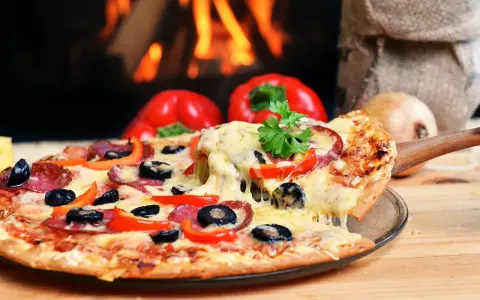 Eine dampfende Pizza mit Salami, Oliven und Paprika, perfekt für den Mitternachtssnack zur Hochzeit, vor einem knisternden Kaminfeuer.