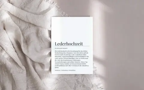 Ein Blatt Papier mit dem Text "Lederhochzeit" und einer Erklärung liegt auf einem hellen Stoff. Der Text beschreibt die Bedeutung der ledernen Hochzeit als Symbol für eine gefestigte Partnerschaft.