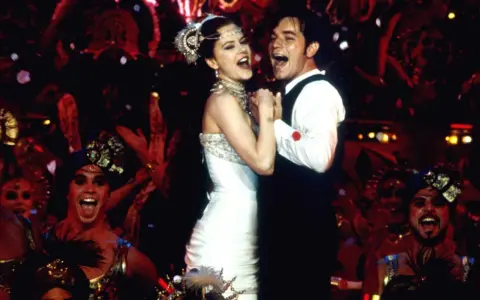 Ein glückliches Paar tanzt, umgeben von einer jubelnden Menge in Kostümen. Ein Moment, der an unvergessliche filmzitate hochzeit erinnert.
