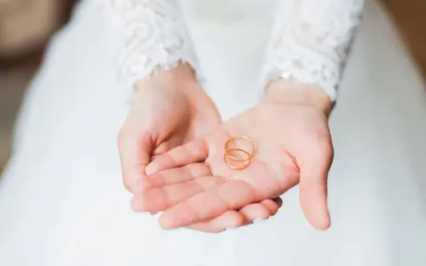 Zwei goldene Eheringe liegen in den Händen einer Braut. Sie sind ein Symbol für ihre bevorstehenden Hochzeitstage und die Namen, die sie für immer verbinden werden.