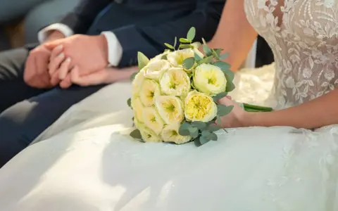 Brautpaar hält Händchen, Brautstrauß mit gelben Rosen. Eine Hochzeit Versicherung gibt Sicherheit für den großen Tag.