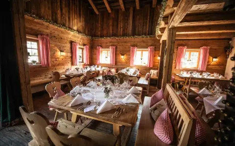 Gemütliche Holzhütte, festlich gedeckte Tische für eine Egerner Alm Hochzeit. Rote Karovorhänge und Blumen schmücken den rustikalen Raum.
