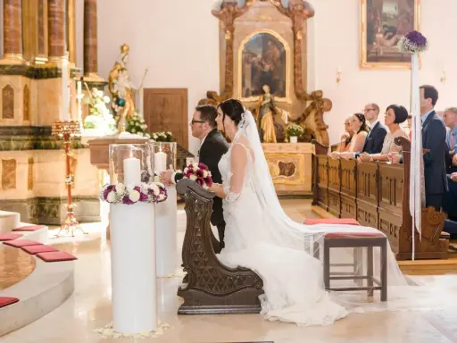Brautpaar kniet vor dem Altar. Sie heiraten kirchlich, nur ein Partner in der Kirche. Gäste sitzen auf den Bänken.