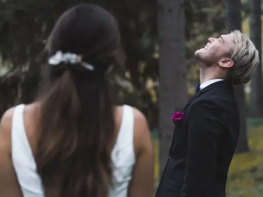 Ein Bräutigam lacht mit geschlossenen Augen in den Himmel, während die Braut ihm den Rücken zukehrt. Vielleicht ist es die Angst vor der Hochzeit, die ihn so überwältigt.