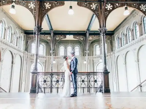 Ein Brautpaar im Stil der 20er Jahre steht sich in einem prachtvollen Gebäude mit Jugendstil-Architektur gegenüber.