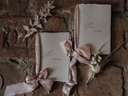 Zwei Büchlein mit zarten Bändern, auf denen "His vows" und "Her vows" steht, bereit, um Eheversprechen zu schreiben.